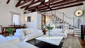 A spacious living area with a high ceiling, wooden beams, a dining area with a table and chairs, and a staircase leading to an upper level. - Le Masque Terrace (Venecia)