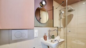 Une salle de bain moderne avec une douche à parois de verre, un lavabo avec un miroir au-dessus et un porte-rouleau de papier toilette.