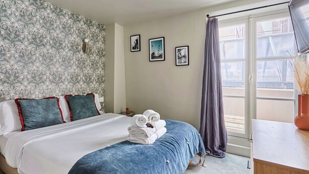 Une chambre d’hôtel avec un lit, une fenêtre avec des rideaux et trois tableaux encadrés accrochés au mur.