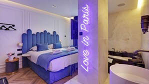 Ein modernes Schlafzimmer mit einem großen Bett, einem Nachttisch, einem an der Wand montierten Fernseher und einem Badezimmer mit Badewanne und Dusche.