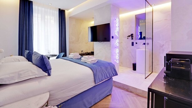Ein modernes Hotelzimmer mit einem großen Bett, einem Flachbildfernseher, einem Spiegel und einem Badezimmer mit Dusche und Toilette.