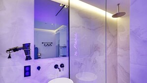 Ein modernes Badezimmer mit Marmorwand, einem großen Spiegel, einer Handbrause und einem Waschbecken mit weißer Schale.