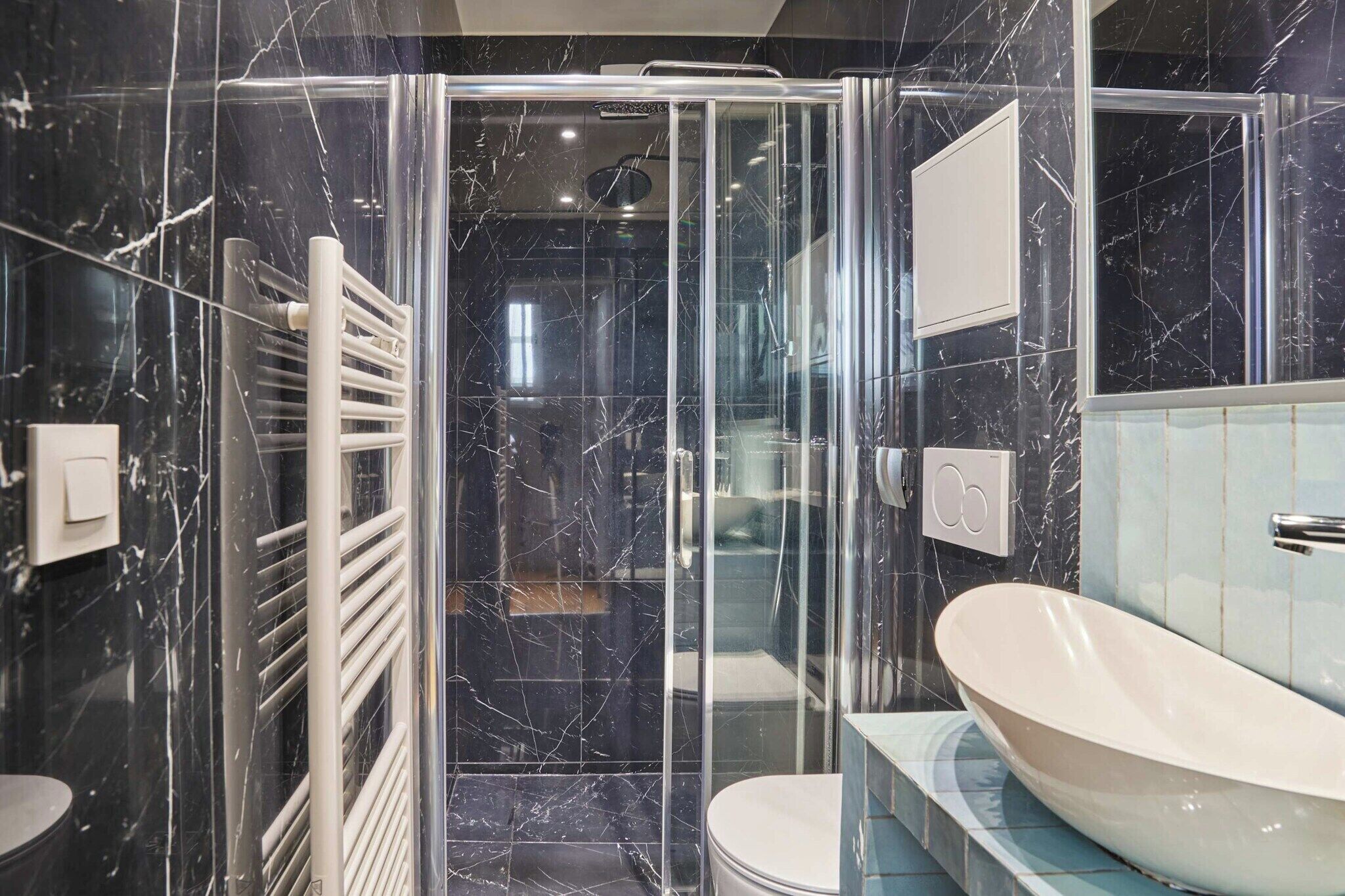 Un baño moderno con ducha envuelta en vidrio, una bañera independiente blanca y un revestimiento de mármol en la pared.