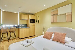 Moderni hotellihuone, jossa on pieni keittonurkkaus, sänky, jossa on kaksi tyynyä, ja pieni sivupöytä.