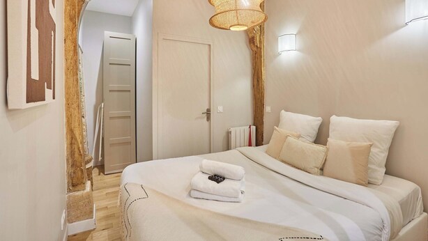 Une chambre avec un grand lit, une arche en bois, un luminaire suspendu et une porte visible au fond.