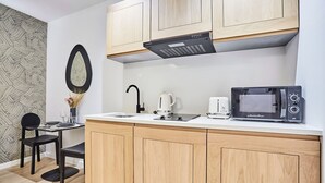 Una cucina compatta con mobili in legno, un forno a microonde, un bollitore e un piccolo angolo ristoro con una sedia e un tavolo.