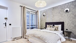Una camera da letto con un letto grande, un termosifone, una finestra con tende, una parete con motivo geometrico e un lampadario.