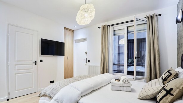 Una camera da letto moderna con un letto grande, una TV a schermo piatto montata a parete, una finestra con tende e una lampada a soffitto.