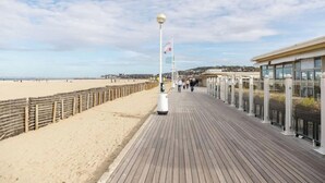A wooden boardwalk leading to a beach with a flagpole and a building with large windows. - Luxury sea view 3BR-2BA with services in Deauville (Deauville)