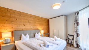 Une chambre d’hôtel avec un mur en bois, un lit avec du linge de maison blanc, deux tables de chevet avec des lampes et une chaise.