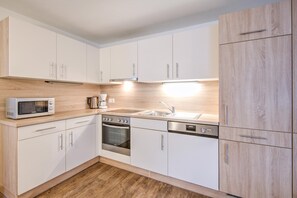 Una cocina moderna con armarios blancos, microondas, horno, lavavajillas y encimera de madera.