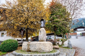 A stone monument with inscriptions, surrounded by a stone circle and a bench, with autumn trees and a building in the background. - Brunner Apartment near the Markbachjoch cable car (Wildschönau)
