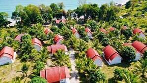 Ein Resort mit mehreren kleinen Häusern mit roten Dächern, umgeben von üppiger Vegetation und einem Strand.