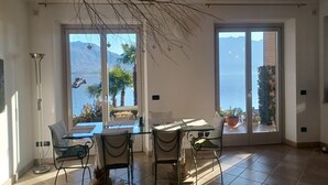 Uma área de refeições com mesa e cadeiras, grandes janelas com vista para o mar e montanhas, e um enfeite de galho pendurado.