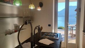 Cozinha com fogão a gás, pia com mangueira e vista para o mar através de uma porta de vidro.