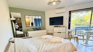 A hotel room with a bed, a TV, a desk, and a balcony with outdoor seating. - Apartment for 4, pool, AC, WiFi, parking, 300m from the beach (Mandelieu-la-Napoule)