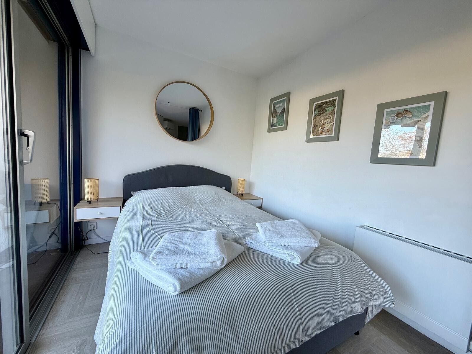 Un dormitorio moderno con cama, lámparas de noche, un espejo y cuadros en la pared.