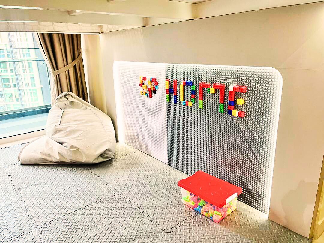 A room with a LEGO wall display spelling "HOME," a white bean bag chair, and a small toy storage box.