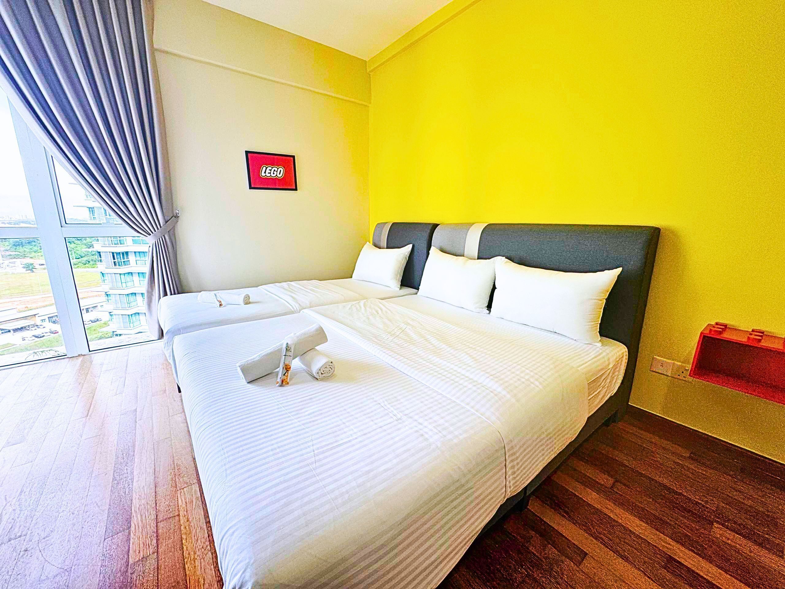 A hotel room with a large bed, a view of the outside, and a LEGO sign on the wall.