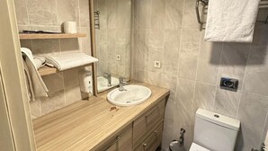 Un baño moderno con tocador de madera, lavamanos, espejo, inodoro y perchero para toallas.