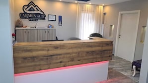 Una mesa de recepción con cubierta de madera y base blanca, un letrero encima y una ventana con cortinas.