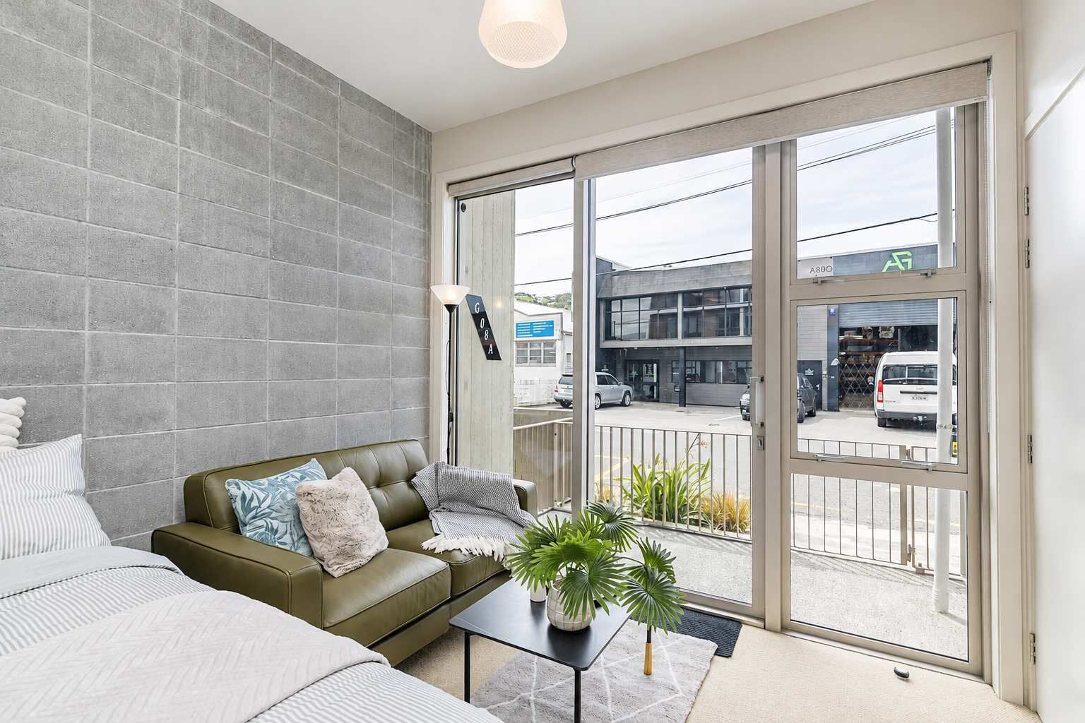 A modern living room with a sofa, a coffee table, and a view of the street through large sliding glass doors.