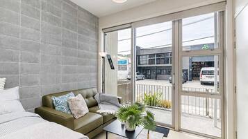 A modern living room with a sofa, a coffee table, and a view of the street through large sliding glass doors.