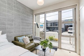 A modern living room with a sofa, a coffee table, and a view of the street through large sliding glass doors.