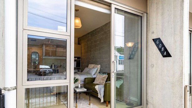 A modern interior with a sliding glass door leading to a bedroom, a visible window with a reflection, and a sign with the number 'G08A' on the wall. - Petone Studio | Balcony + Full Kitchen (Lower Hutt)