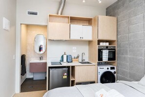 A compact hotel room with a kitchenette, a bed, a washing machine, and a small bathroom.