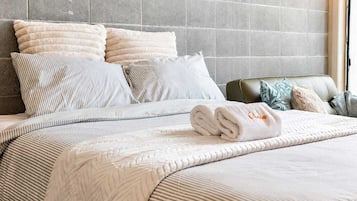 A neatly made bed with a striped bedspread and pillows, a folded towel, and a headboard against a tiled wall.