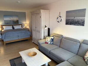 Un dormitorio con cama, armario, mesita de noche con lámpara, sofá, mesa de centro y decoración en la pared.