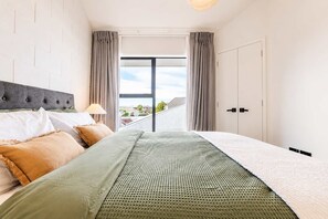 A hotel room with a bed, a window with curtains, a view of the outside, and a door. - 1BR with Courtyard + Parking | Near CBD (Christchurch)
