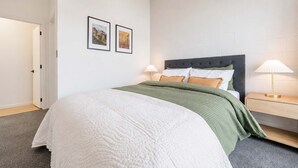 A bedroom with a bed, two bedside lamps, a nightstand, and two framed pictures on the wall. - 1BR with Courtyard + Parking | Near CBD (Christchurch)