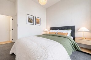 A bedroom with a bed, two bedside lamps, a nightstand, and two framed pictures on the wall. - 1BR with Courtyard + Parking | Near CBD (Christchurch)