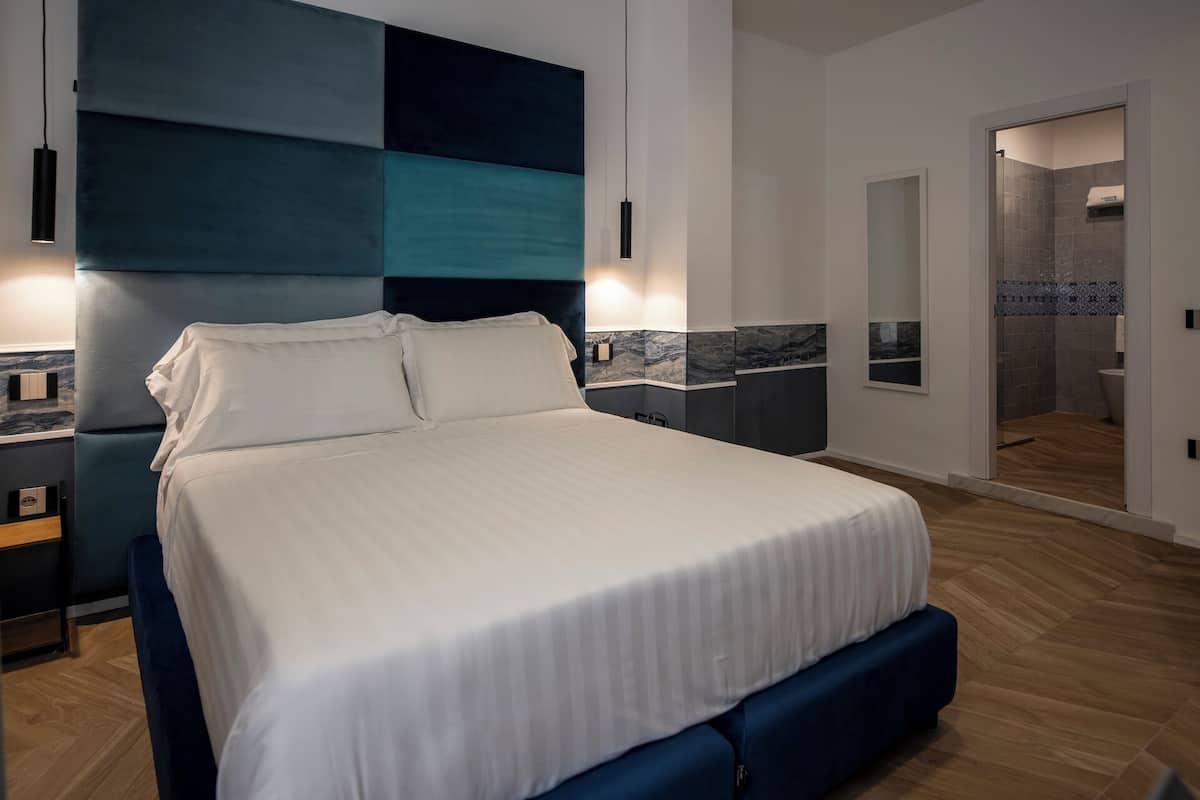 A modern bedroom with a large bed, a headboard with a geometric design, a nightstand, and a bathroom visible through an open door.