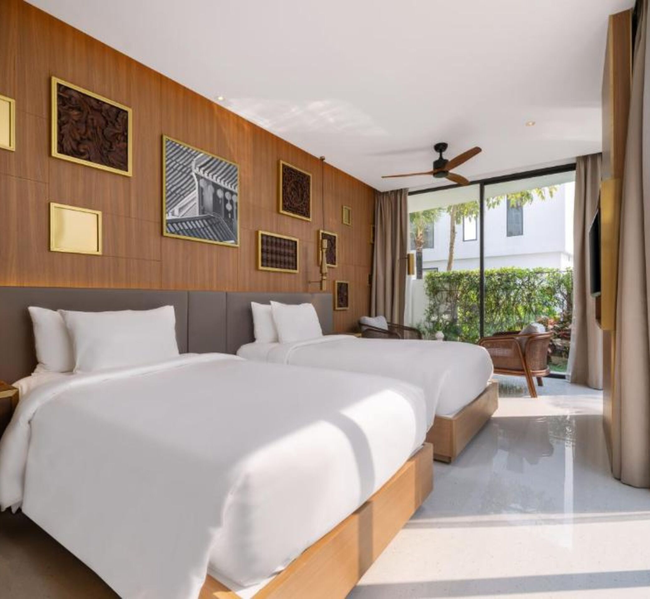 A modern hotel room with two beds, a ceiling fan, and a view of the outdoors.