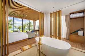 Een moderne hotelkamer met een groot bed, een badkuip, een bank en uitzicht op palmbomen.
