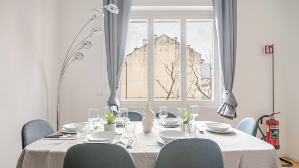 Un coin repas avec une table dressée pour quatre personnes, un vase et une plante en pot.