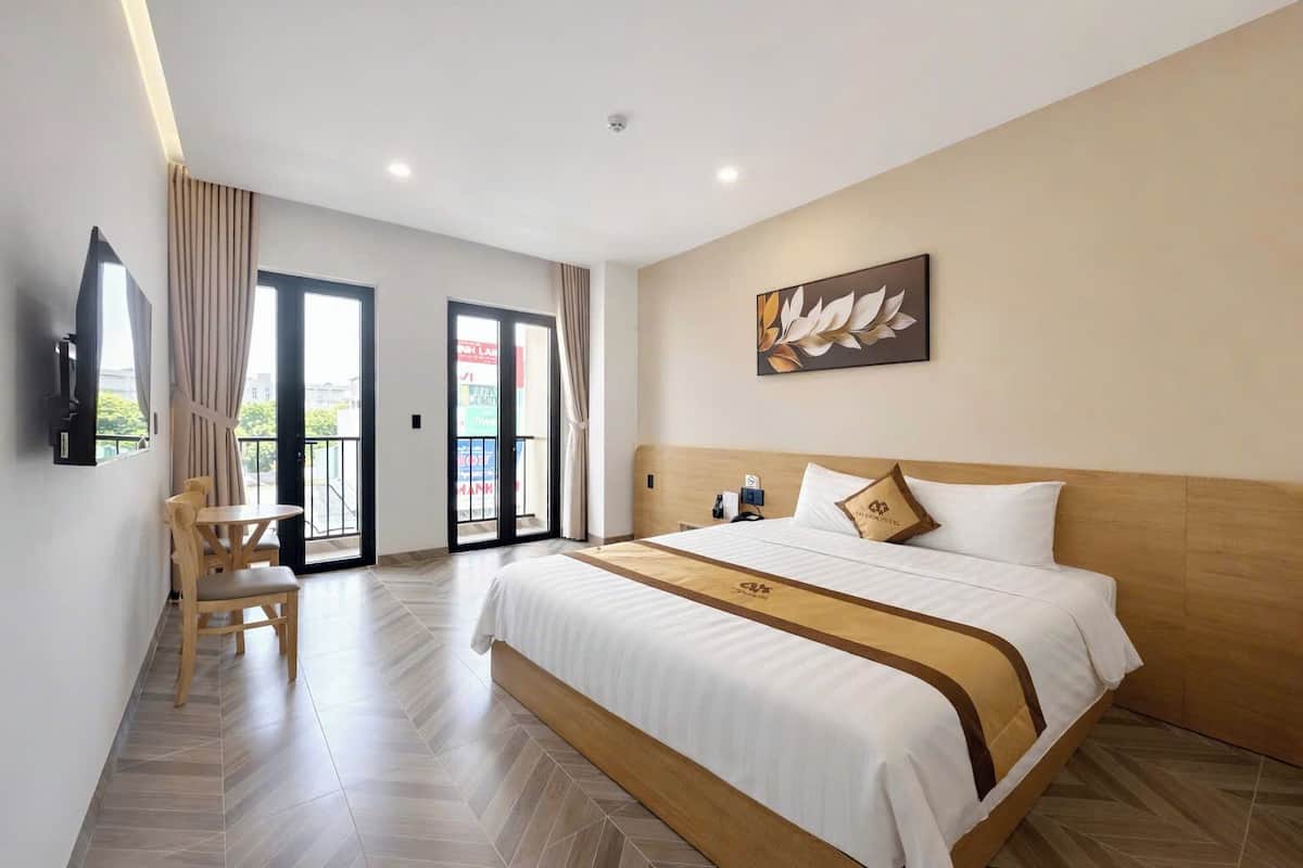 A hotel room with a bed, a desk, a chair, a TV, and a balcony with curtains.