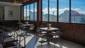 Un restaurante con amplios ventanales, paredes de madera y un ventilador de techo. Mesas y sillas dispuestas para comer.