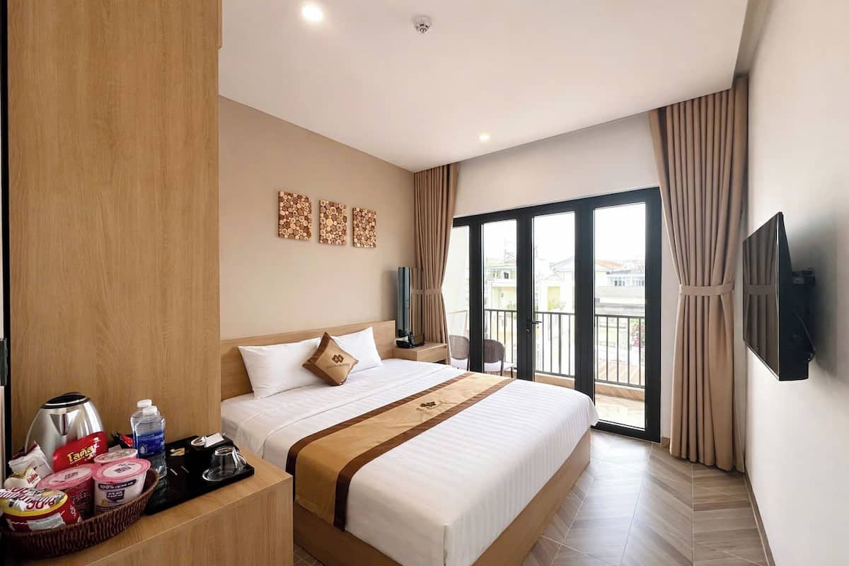 A hotel room with a large bed, a flat-screen TV, a balcony with curtains, and a wooden panel on the left wall.
