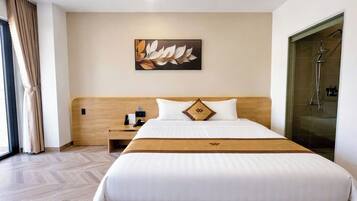 A hotel room with a large bed, a wooden headboard, a nightstand with a phone, a wall-mounted artwork, and a shower area.
