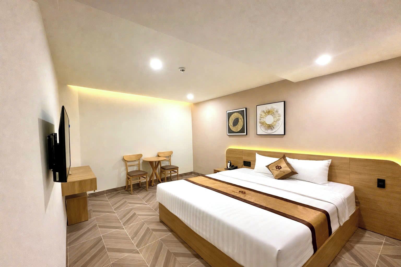 Ein Hotelzimmer mit einem großen Bett, einem Schreibtisch, zwei Stühlen, einem Fernseher und zwei an der Wand befestigten Kunstwerken.