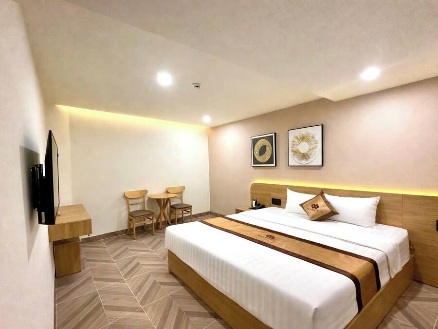 Quarto de hotel com uma cama grande, uma escrivaninha, duas cadeiras, uma TV e duas obras de arte penduradas na parede.