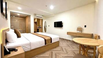 A hotel room with a bed, bedside table, desk, chair, TV, and a herringbone-patterned floor.