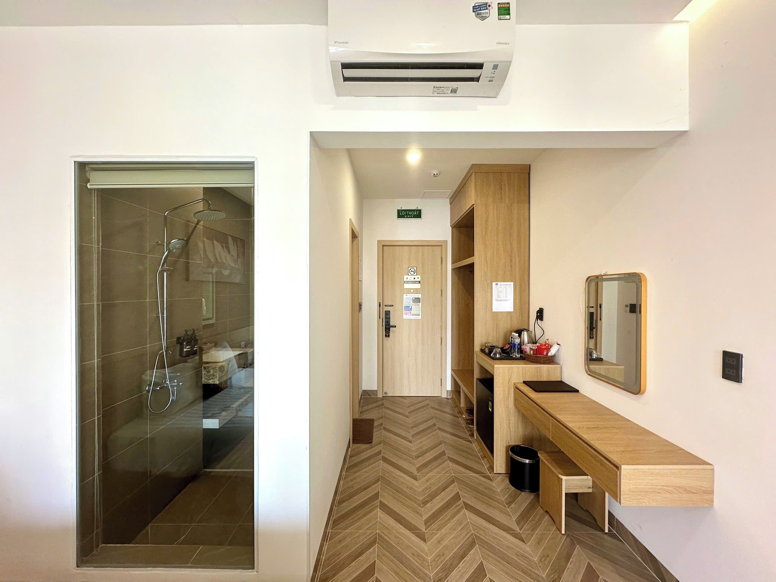 Een hotelbadkamer met een glazen douchecabine, een houten wastafelmeubel met spiegel en een vloer met een herringbone-patroon.