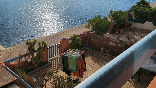 A balcony with a view of a calm body of water, a dock with boats, and a row of buildings in the background. - Large studio with view of Salses lake (Le Barcarès)