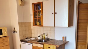 A compact kitchen with wooden cabinets, a built-in microwave, and a sink. - Large studio with view of Salses lake (Le Barcarès)