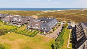 An aerial view of a residential area with houses, a parking lot, and a view of the sea.